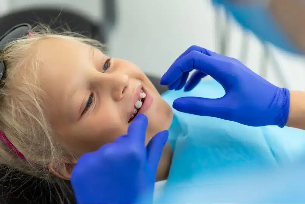 A smiling young girl having her dental retainer checked by a professional wearing blue gloves.