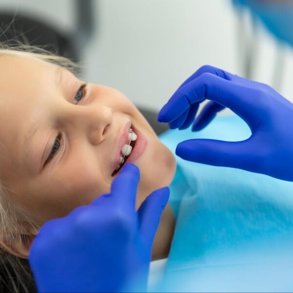 A smiling young girl having her dental retainer checked by a professional wearing blue gloves.
