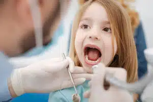 A little girl with her mouth open during a dental procedure at a pediatric office.