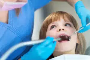 A young girl receiving a dental checkup from a dentist using a mirror and tool.