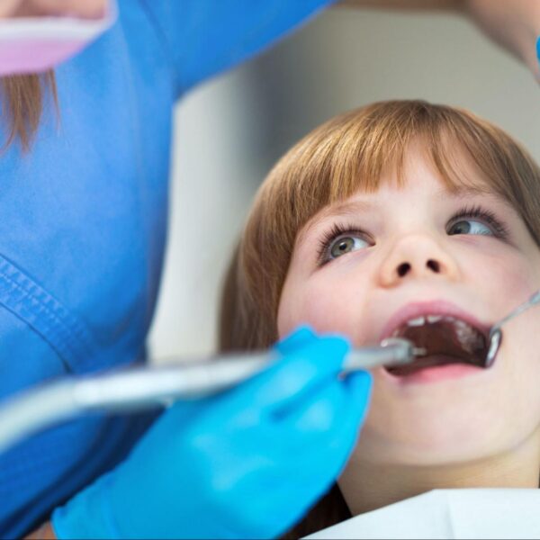 A young girl receiving a dental checkup from a dentist using a mirror and tool.