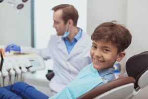 A young boy smiling in a dental chair with the dentist working in the background