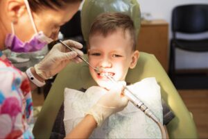 A young boy sitting in a dental chair while a dentist uses tools to check his teeth