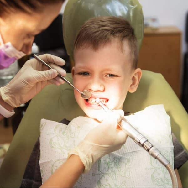 A young boy sitting in a dental chair while a dentist uses tools to check his teeth