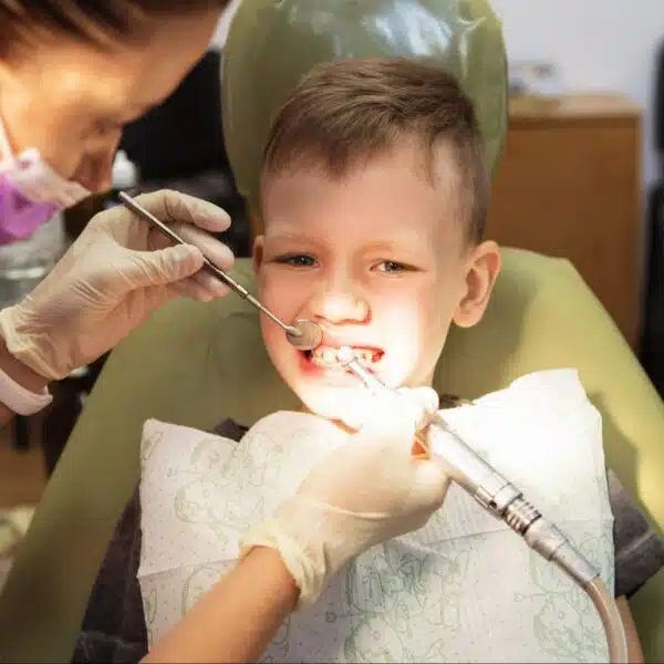 A young boy sitting in a dental chair while a dentist uses tools to check his teeth