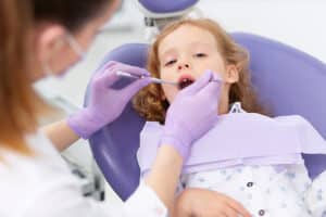A young child sitting in a purple dental chair during a dental examination