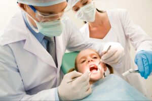 A young girl receiving a dental exam from a dentist and assistant wearing masks